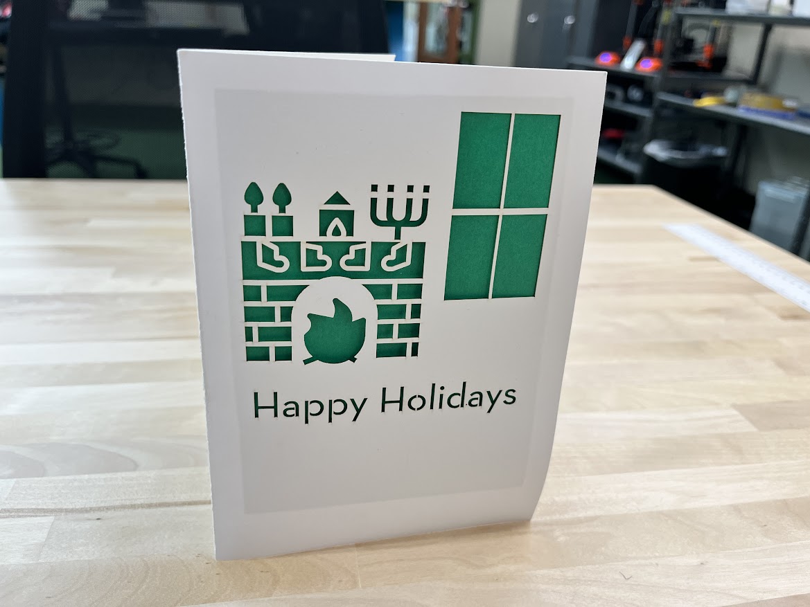 A photo of a holiday card that has been laser cut with a design of a fireplace and window.