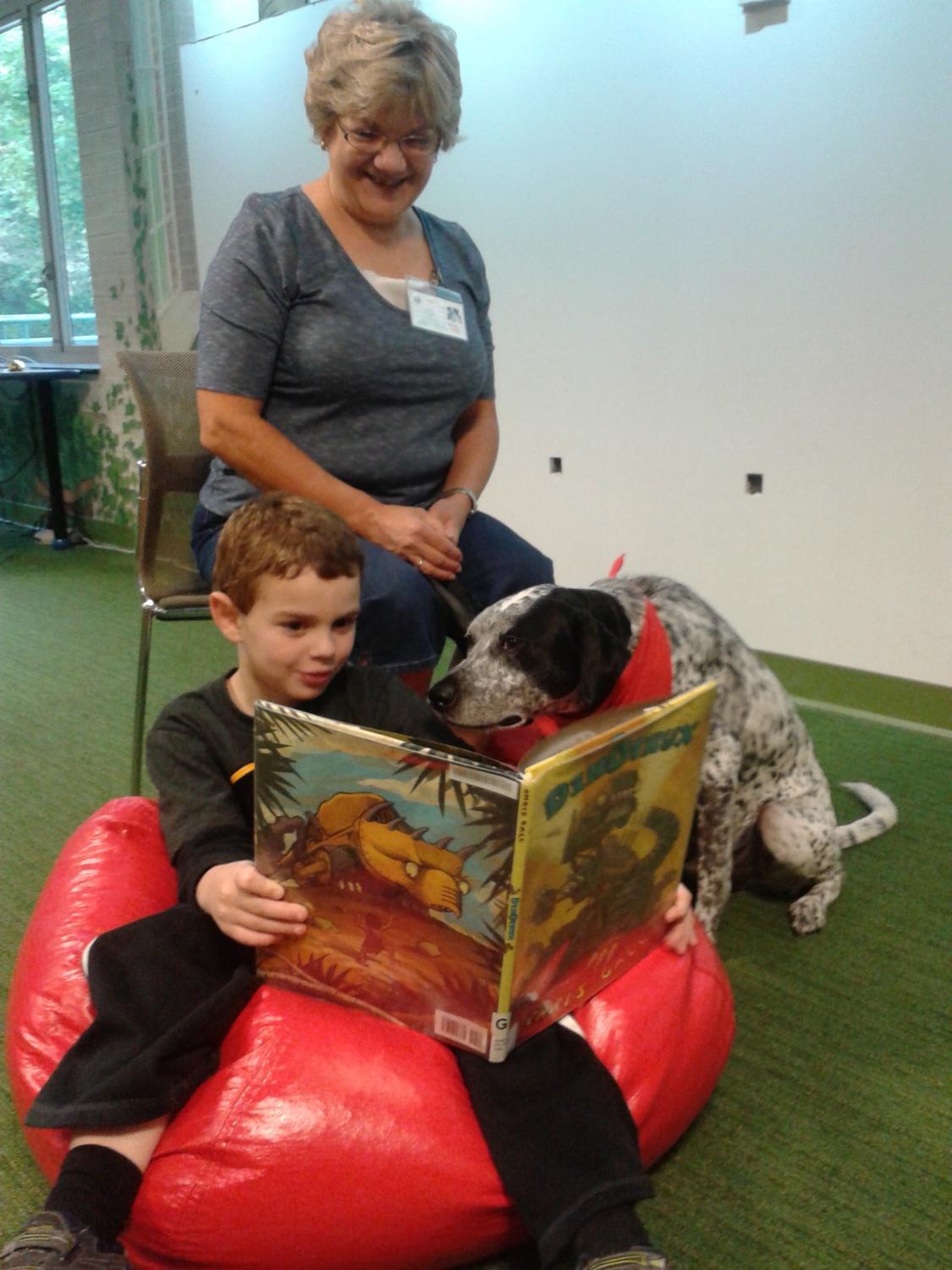 child sitting on a bean bag chair while reading a book to a dog