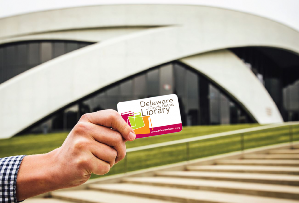 a hand holding a delaware county library card in front of the national veterans memorial and museum